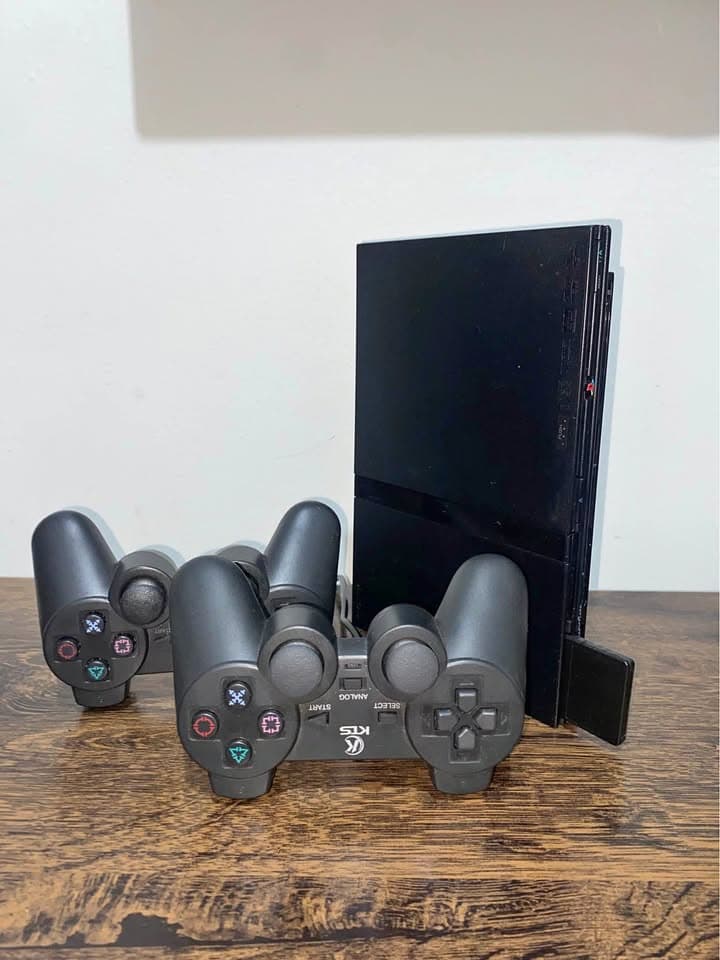 PlayStation 2 slim preto com dois controles sem fio ao lado